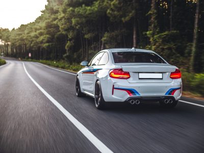 White Sedan Driving Highway Across Forest